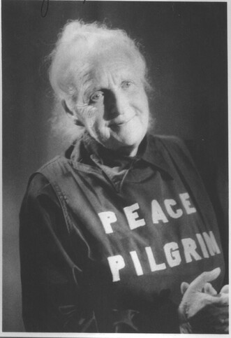 A black and white photo of a woman known by the moniker, "Peace Pilgrim" with the words, "Peace Pilgrim" printed on her shirt.